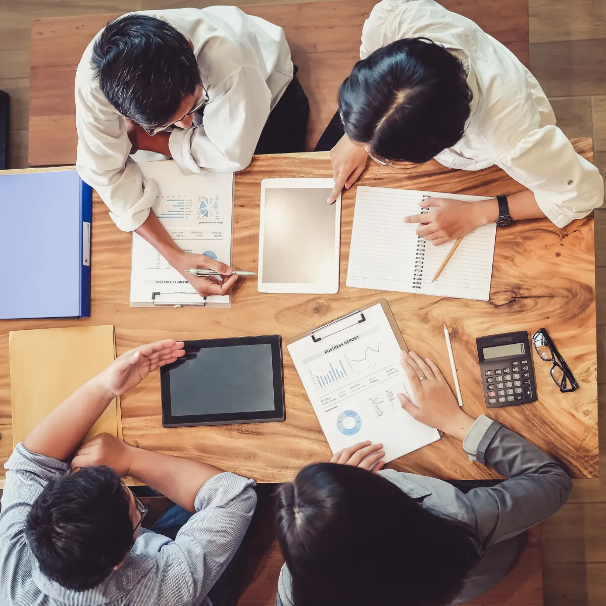 Trabalho em grupo visto de cima, com relatórios espalhados na mesa
